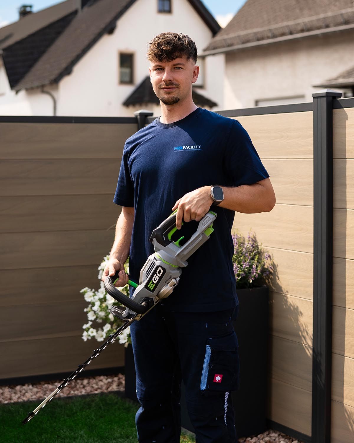 Mike Reidenbach, Inhaber von MRX FACILITY, mit Akku-Heckenschere im Garten eines Wohnhauses